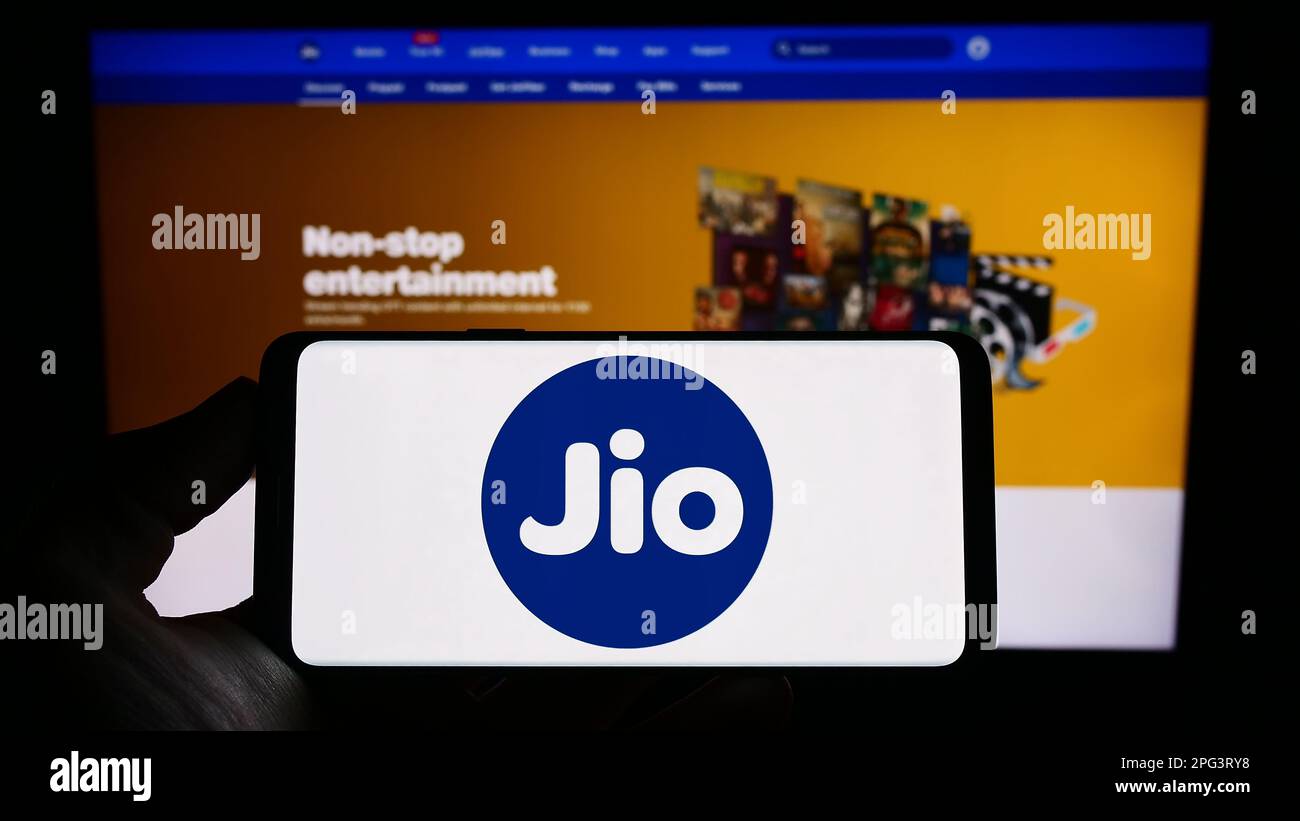 Person holding cellphone with logo of Indian telecommunications company Reliance Jio on screen in front of webpage. Focus on phone display. Stock Photo