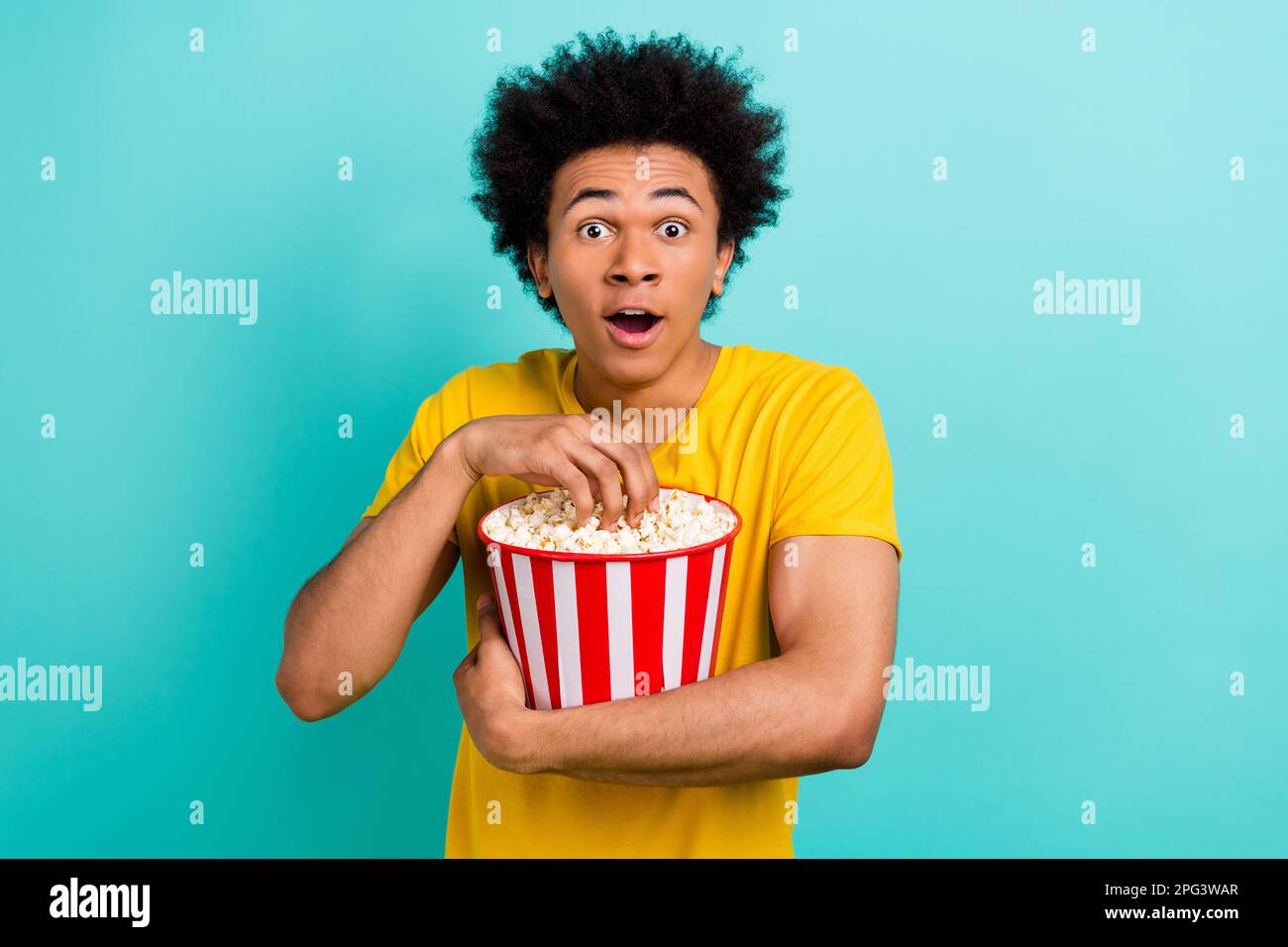 Portrait of impressed handsome man open mouth hold eat popcorn isolated on teal color background Stock Photo