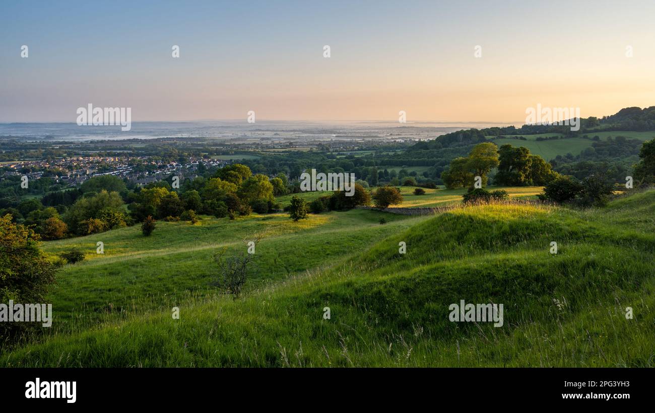 Dawn light falls on Broadway village and the misty landscape of the Vale of Evesham as seen from Broadway Hill on the Cotswold Edge in Worcestershire. Stock Photo