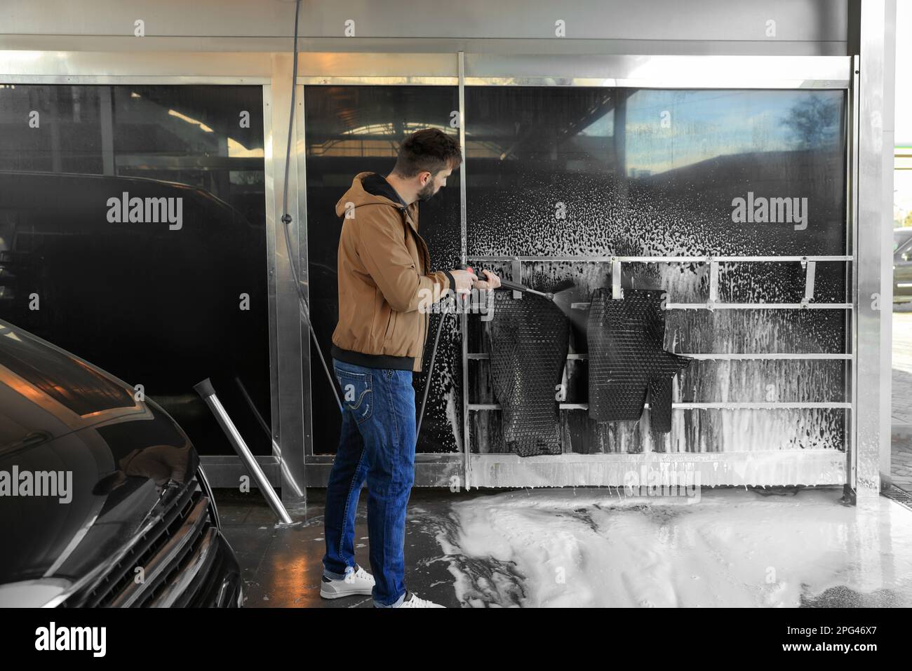 Man cleaning auto mats with high pressure water jet at selfservice car