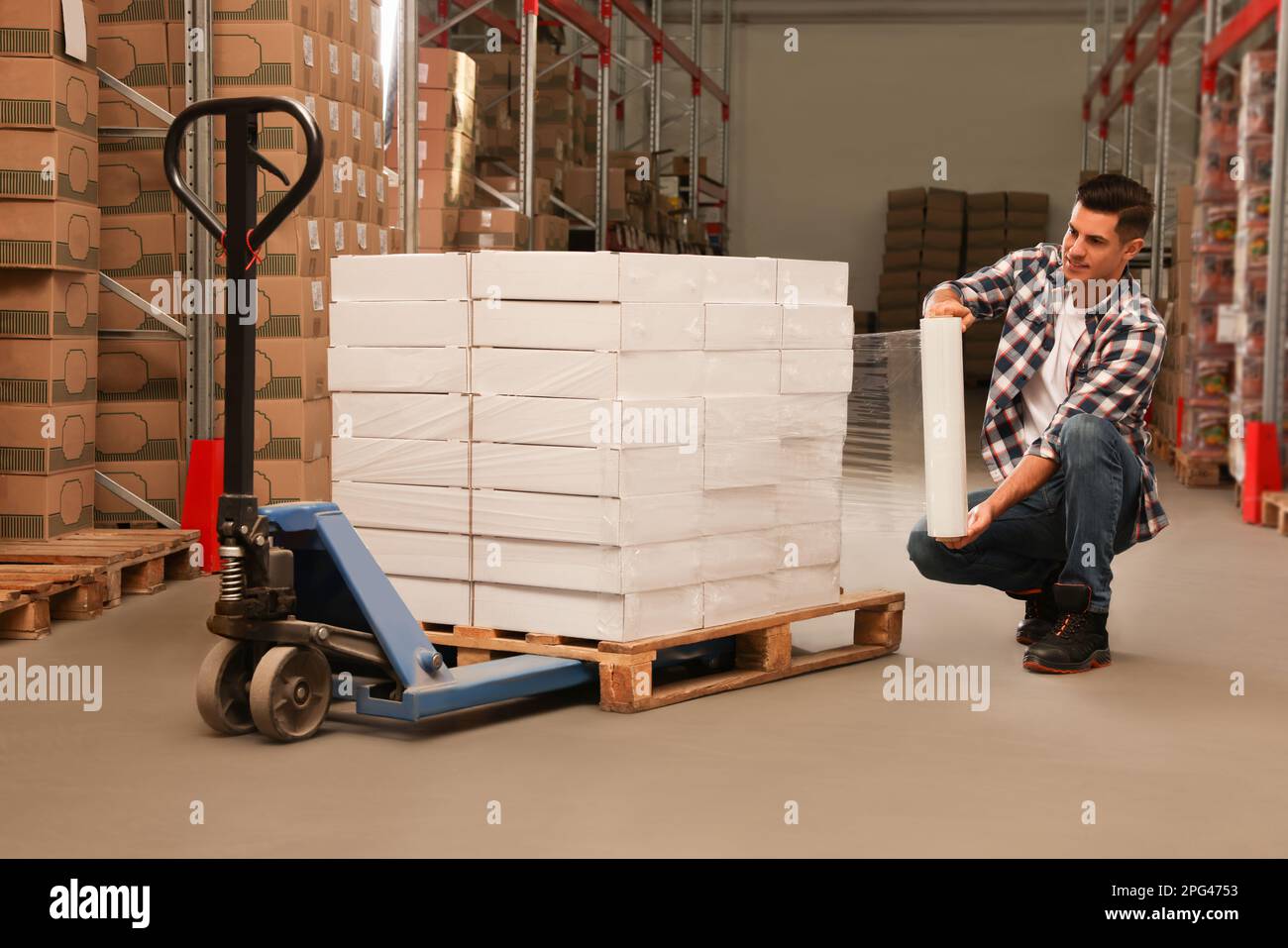 Worker wrapping boxes in stretch film at warehouse Stock Photo
