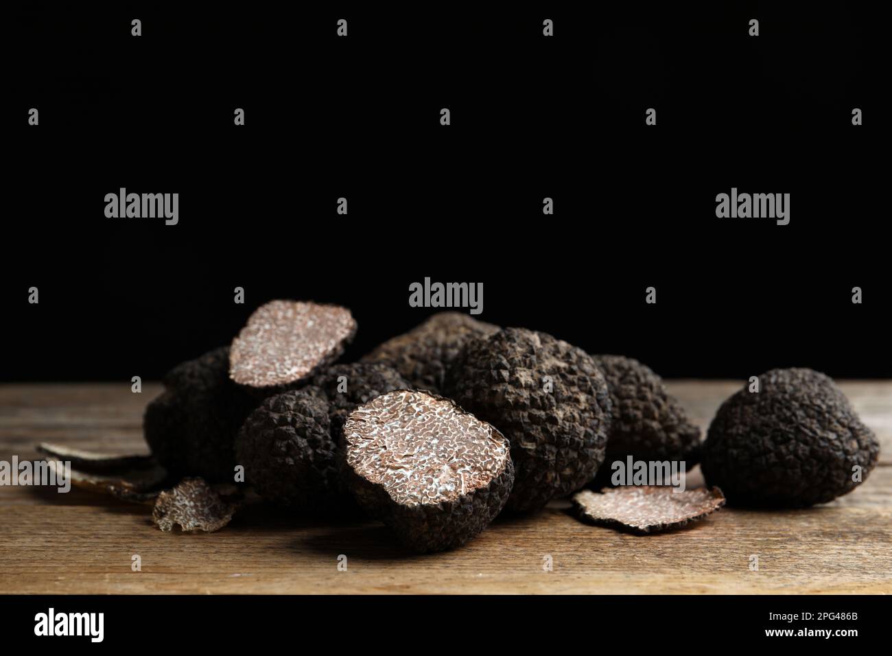 Whole and cut truffles on wooden table against black background Stock Photo