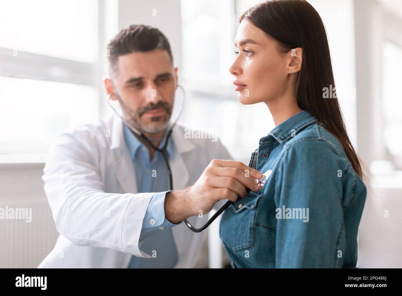 Lady coming to clinic for checkup, male doctor using stethoscope