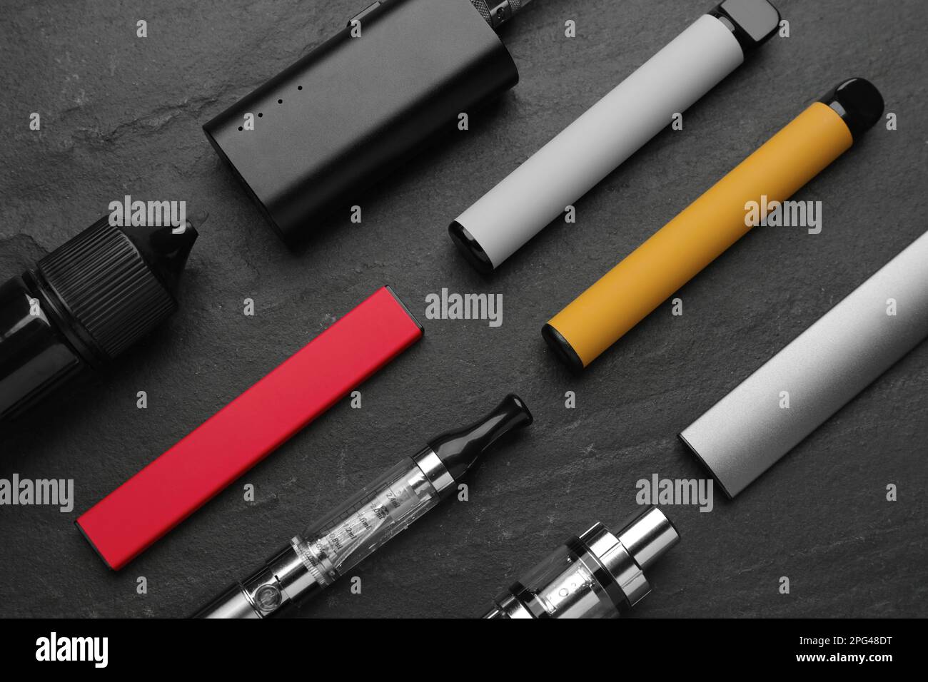 Many electronic smoking devices on black background, flat lay Stock