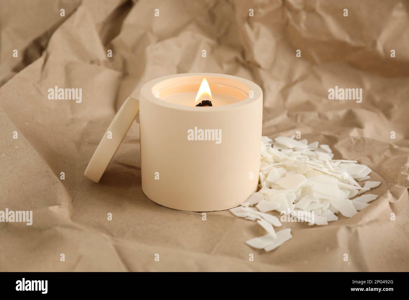Burning soy candle and wax flakes on crumpled kraft paper Stock Photo