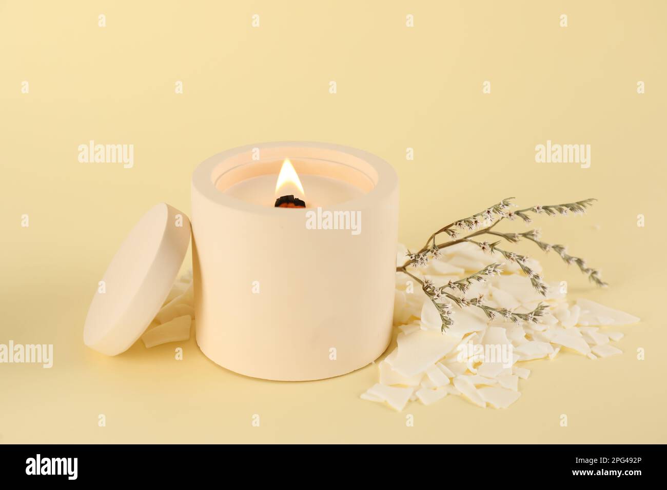 Burning soy candle, wax flakes and statice twig on beige background
