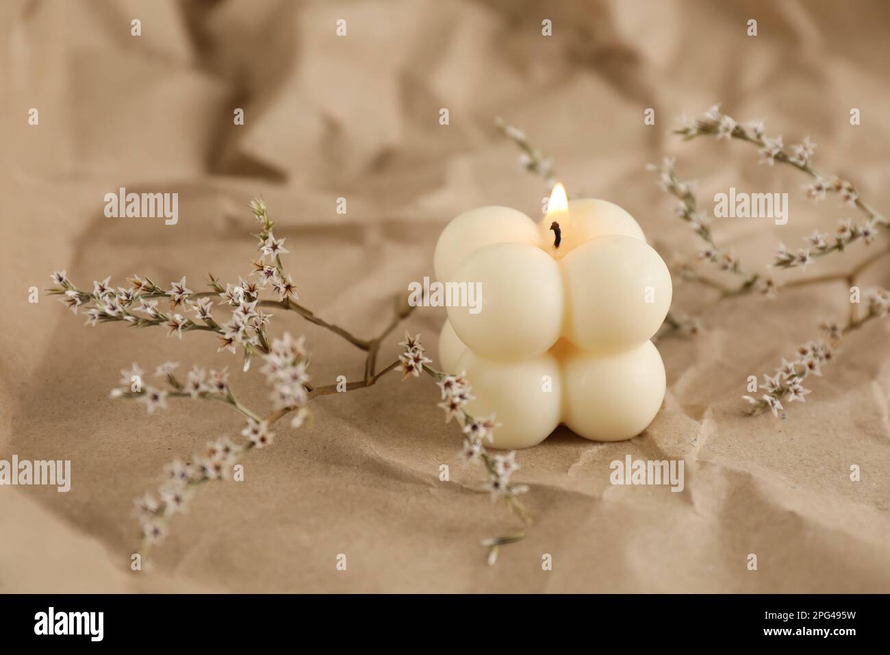 Burning soy candle and statice twigs on crumpled kraft paper Stock