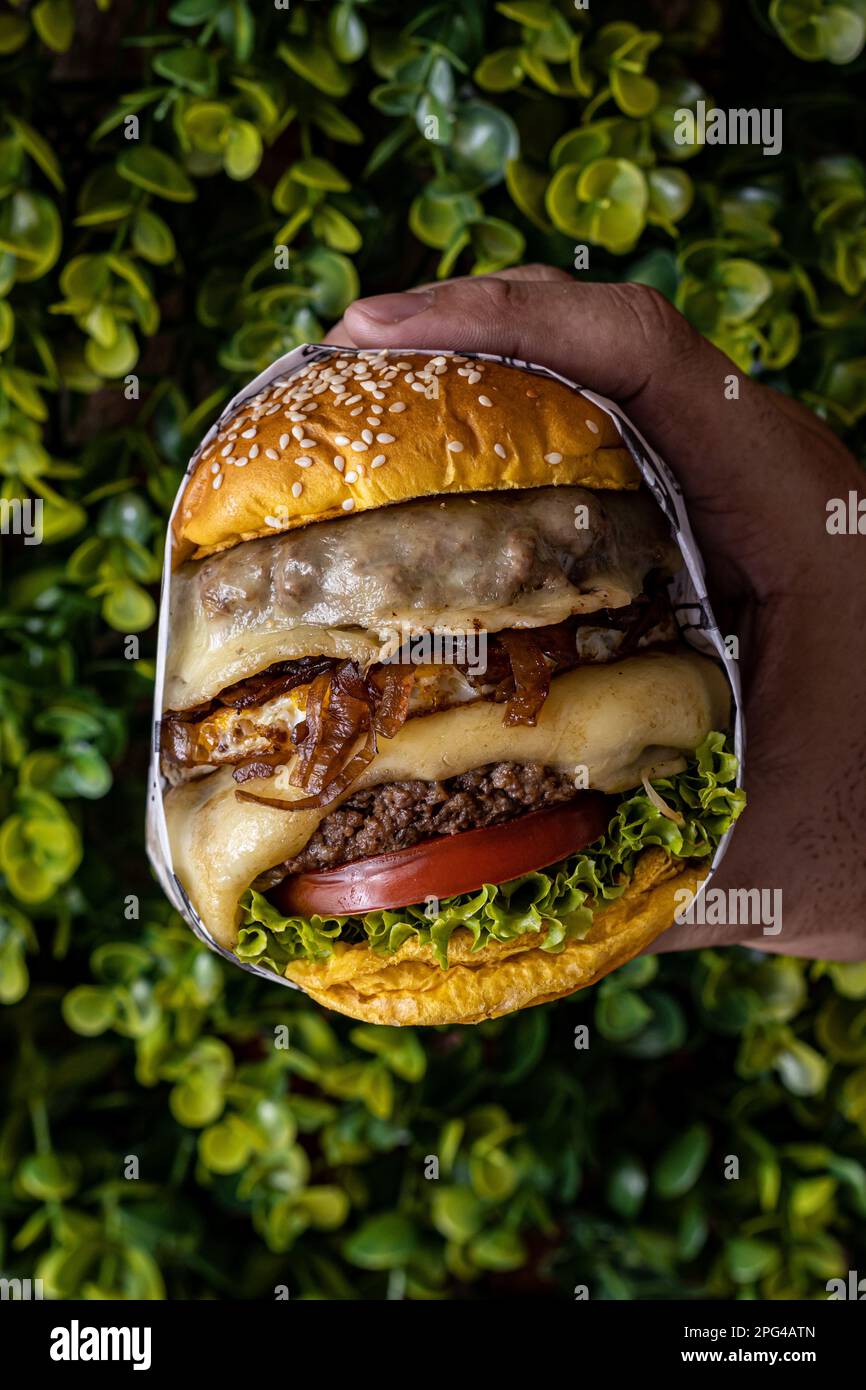 An appetizing hamburger wrapped in foil paper, held by a male hand Stock Photo