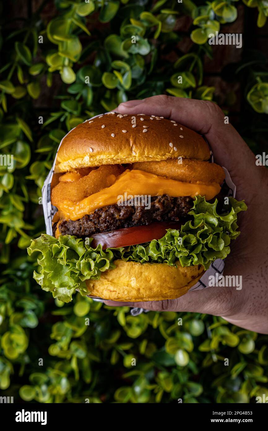 An appetizing hamburger wrapped in foil paper, held by a male hand Stock Photo
