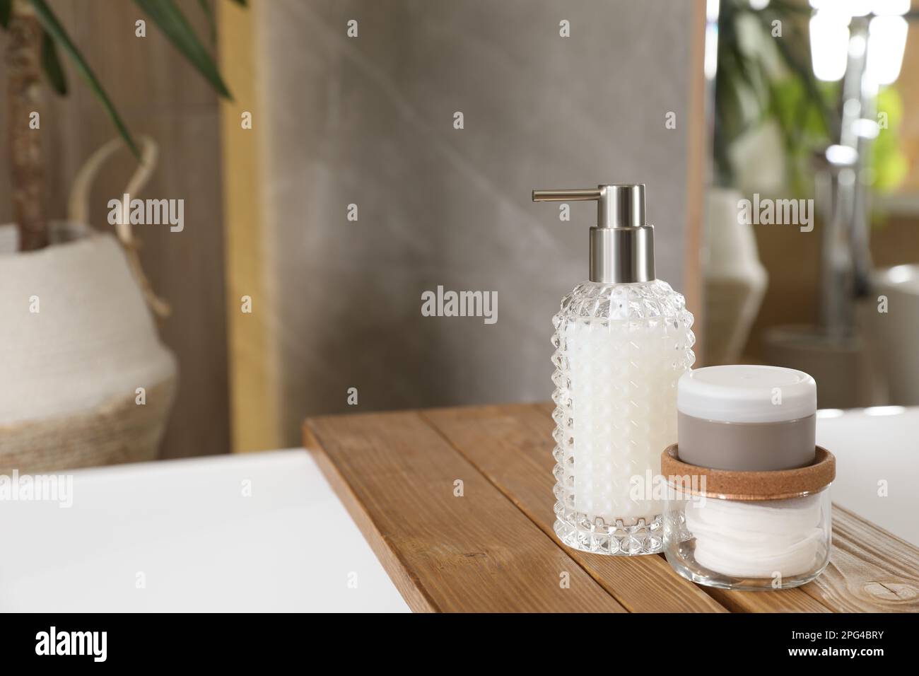 White tub with soap dispenser, cotton pads and jar in bathroom, space ...