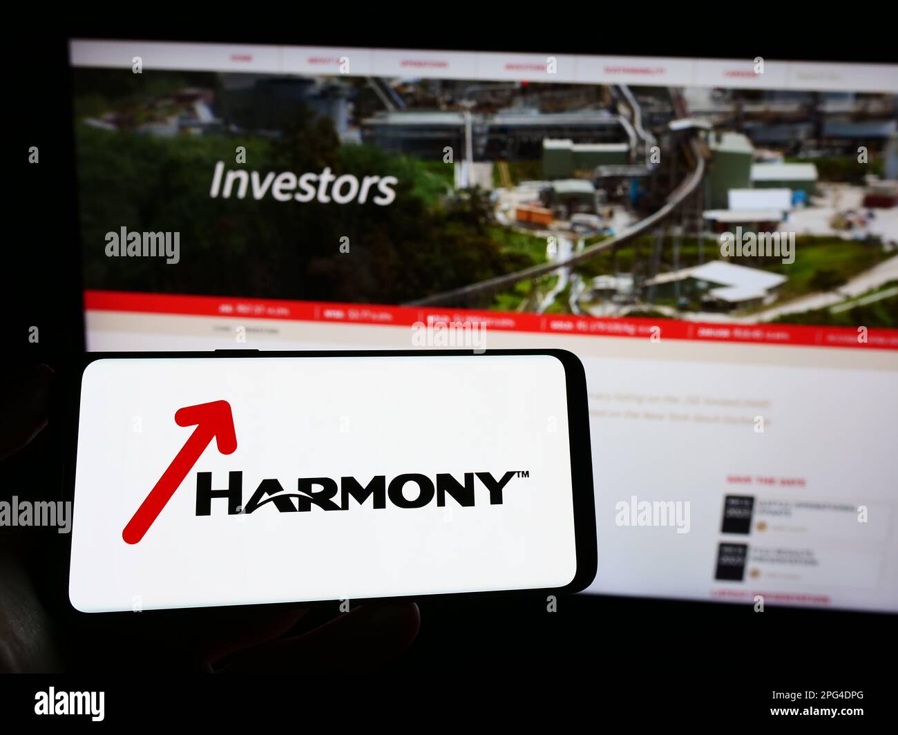 Person holding smartphone with logo of company Harmony Gold Mining Co. Ltd. on screen in front of website. Focus on phone display. Stock Photo