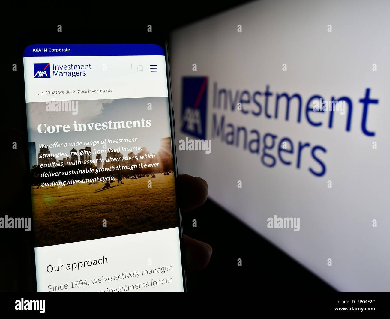 Person holding smartphone with web page of investment company Axa Investment Managers on screen with logo. Focus on center of phone display. Stock Photo