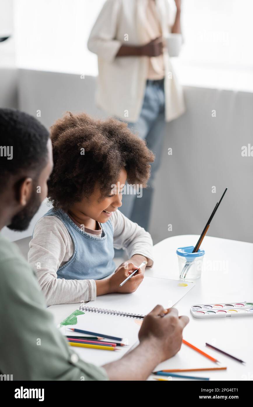 Positive african american kid painting with father at home,stock image Stock Photo