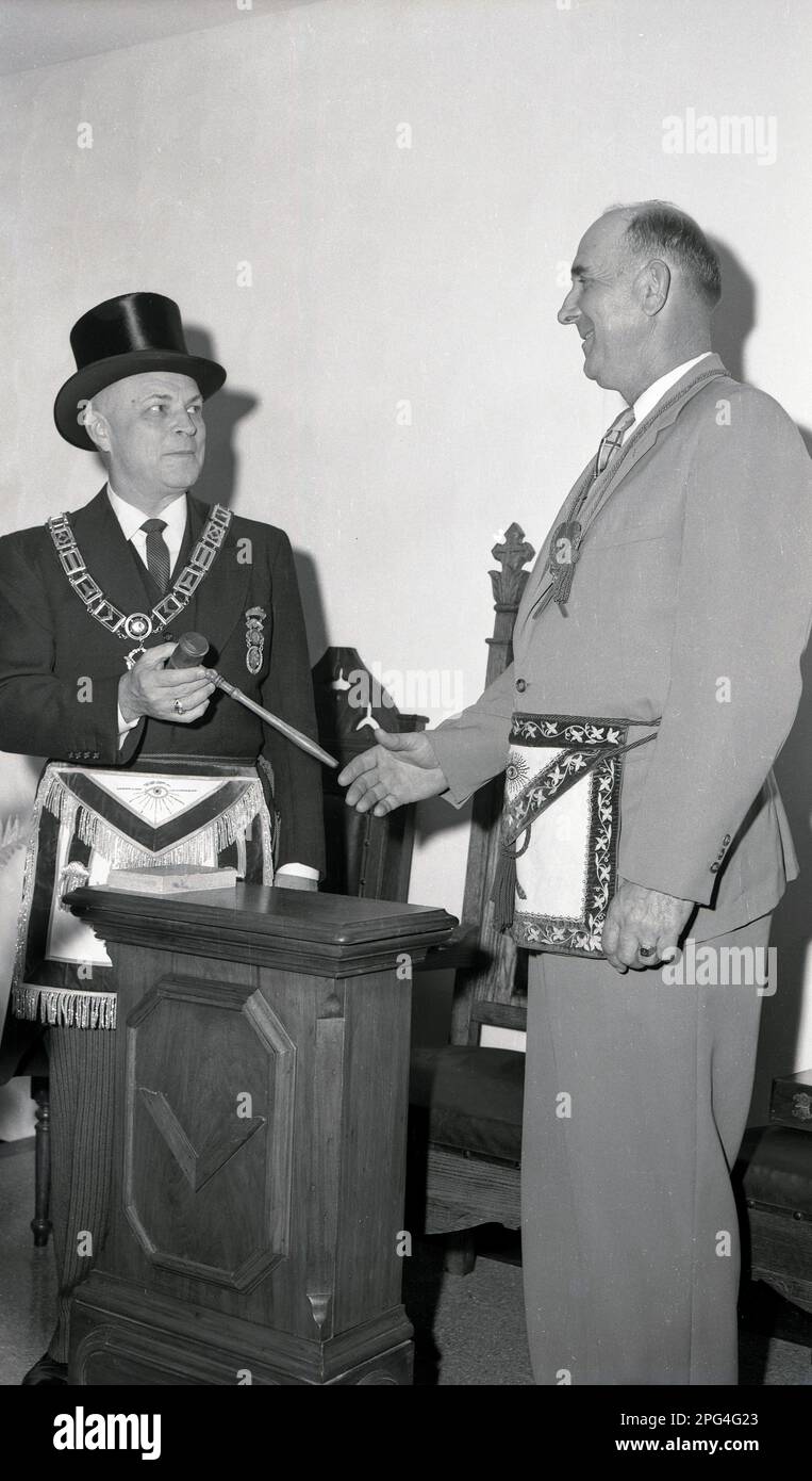1940s, historical, freemasons ceremony, two men, one the worshipful master is wearing a hat and chain handing a masonic mallet or gavel to another man, USA. Stock Photo