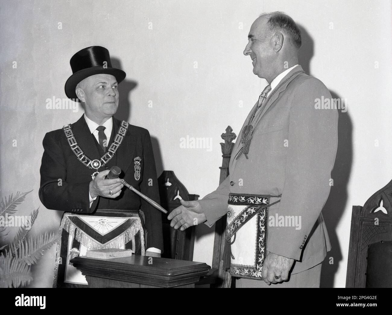 1940s, historical, freemasons ceremony, two men, one the worshipful master is wearing a hat and chain handing a masonic mallet or gavel to another man, USA. Stock Photo