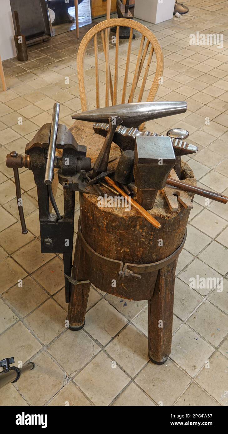 Traditionally worn fine art silversmith tools on an old wooden craftsman workbench in a workshop. Hammer and anvil. Stock Photo