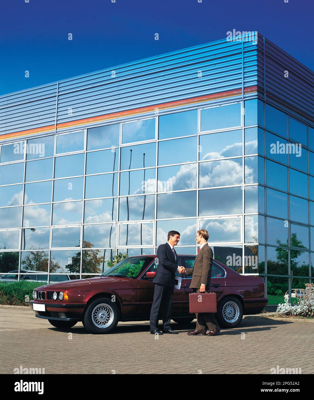Business executives standing outside modern commercial building with vintage BMW car. Stock Photo