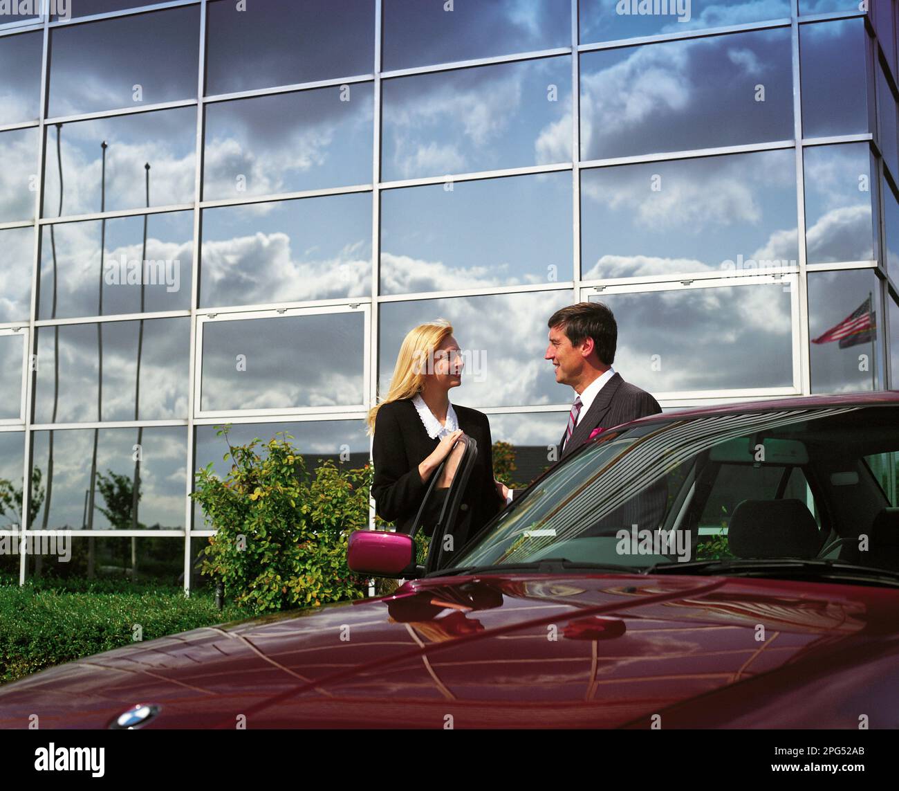 Man & woman business executives standing by car outside commercial building. Stock Photo