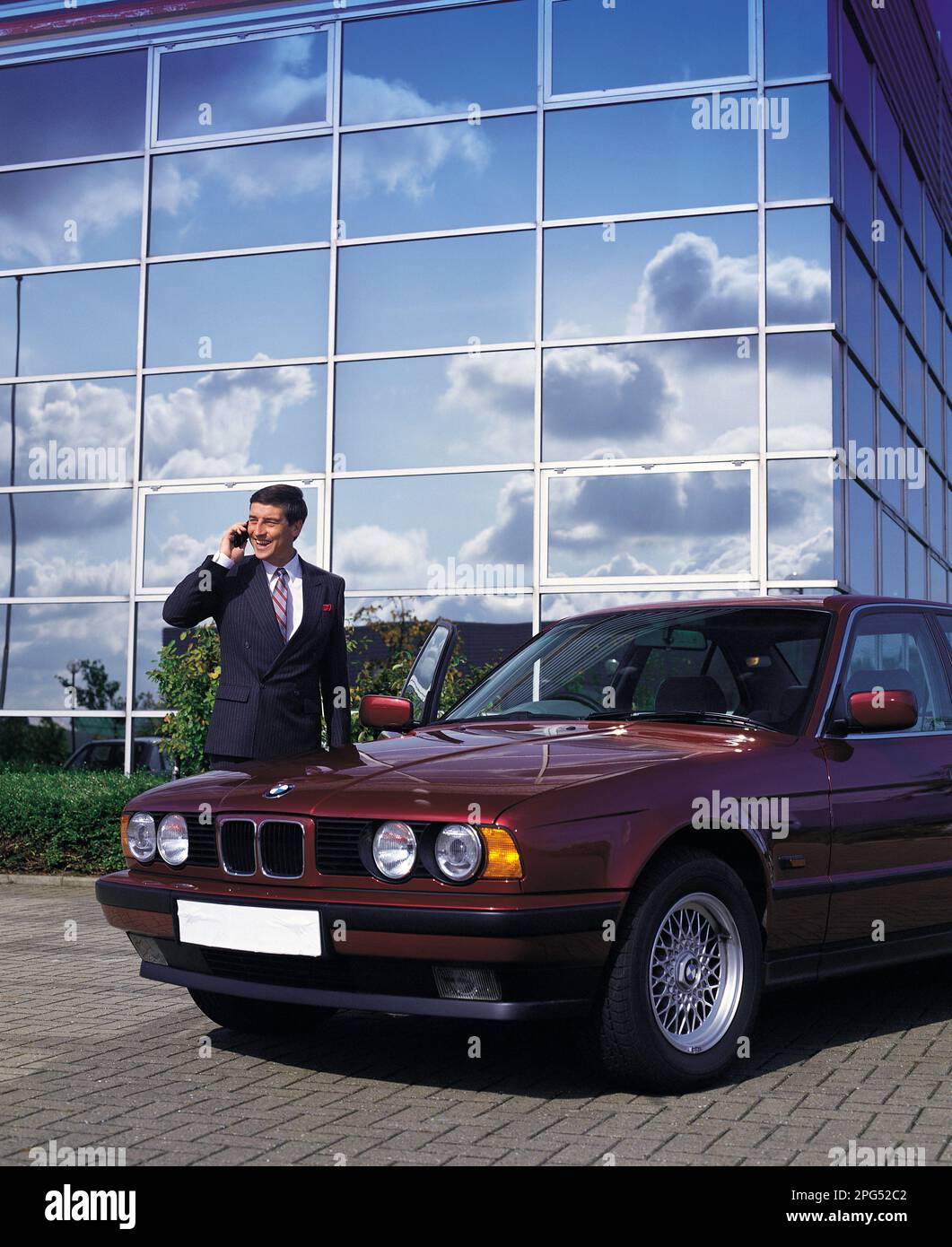 Businessman with cell phone standing by a vintage BMW car outside office building. Stock Photo