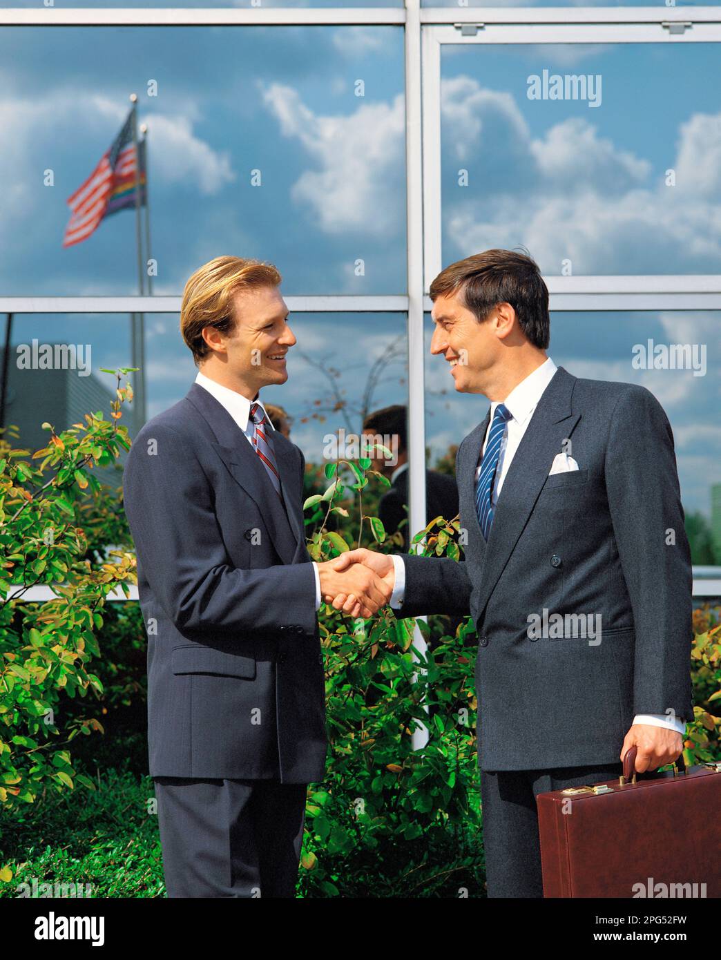 Two businessmen shaking hands, standing outside a commercial building. Stock Photo