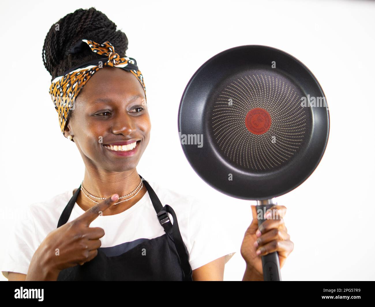 Young female chef showing and pointing a non stick pan while smiling. Isolated on a white