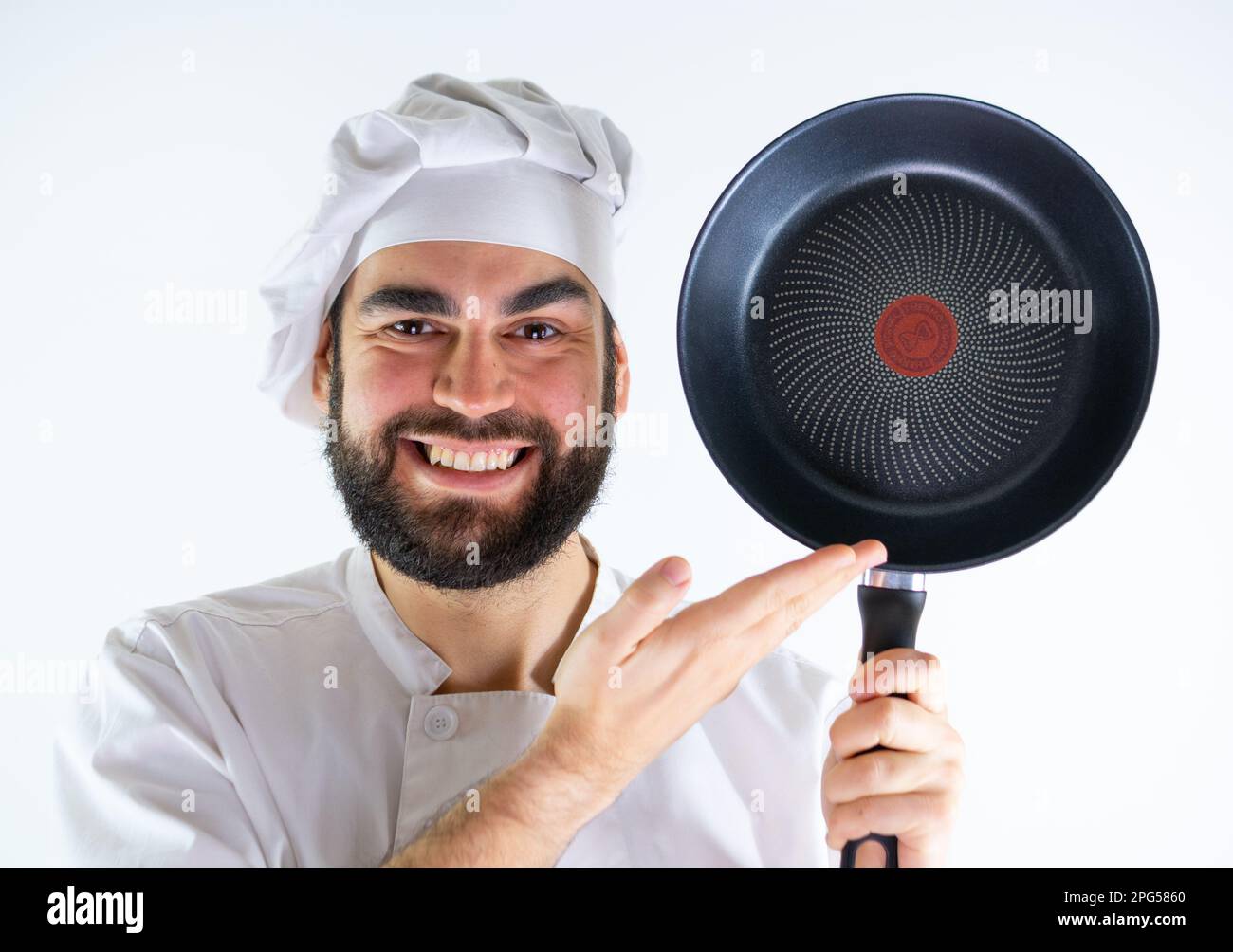 Young male chef showing a non stick pan while smiling and looking at