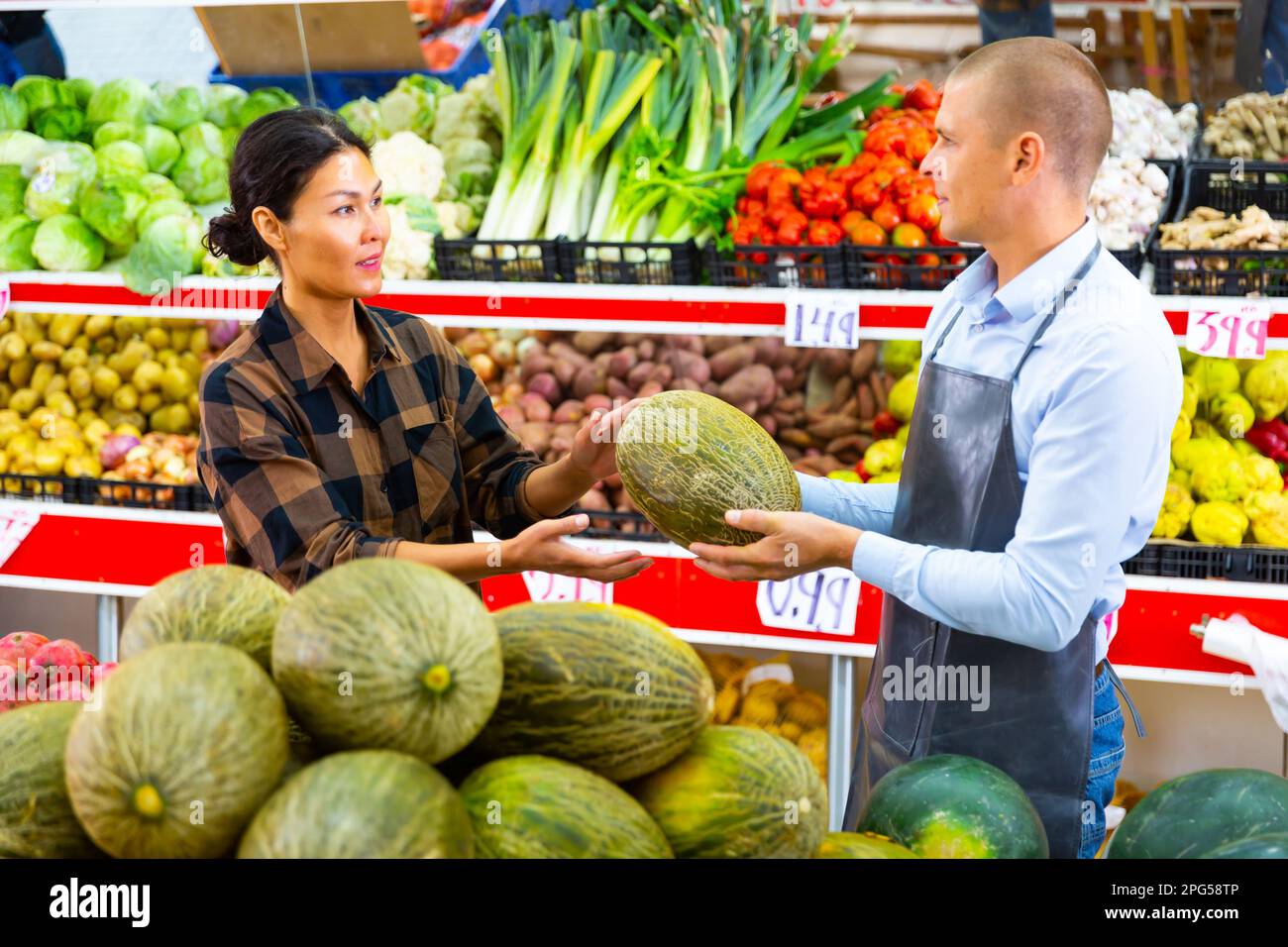 Greengrocer worker explaining woman how to choose melon Stock Photo Alamy
