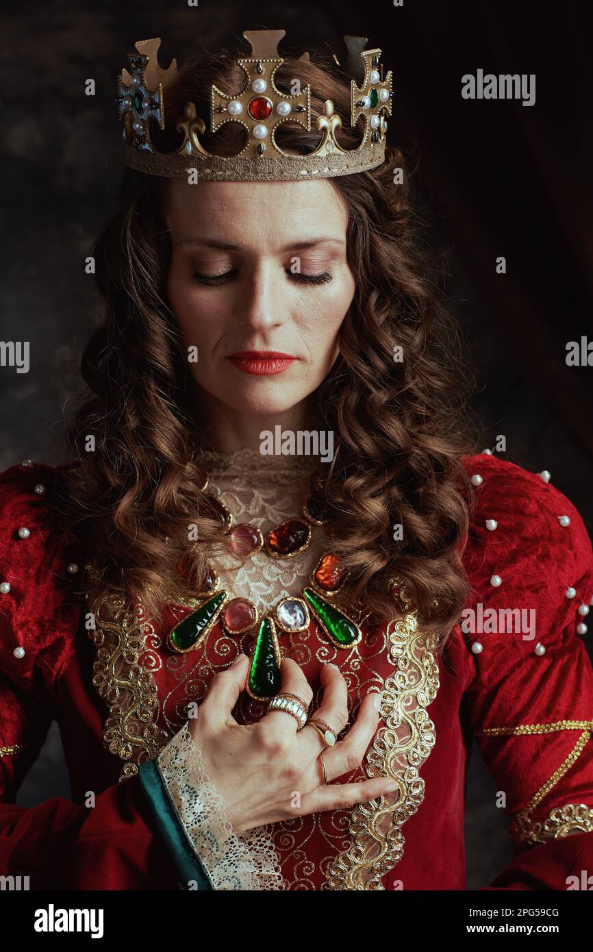 medieval queen in red dress with crown on dark gray background. Stock Photo