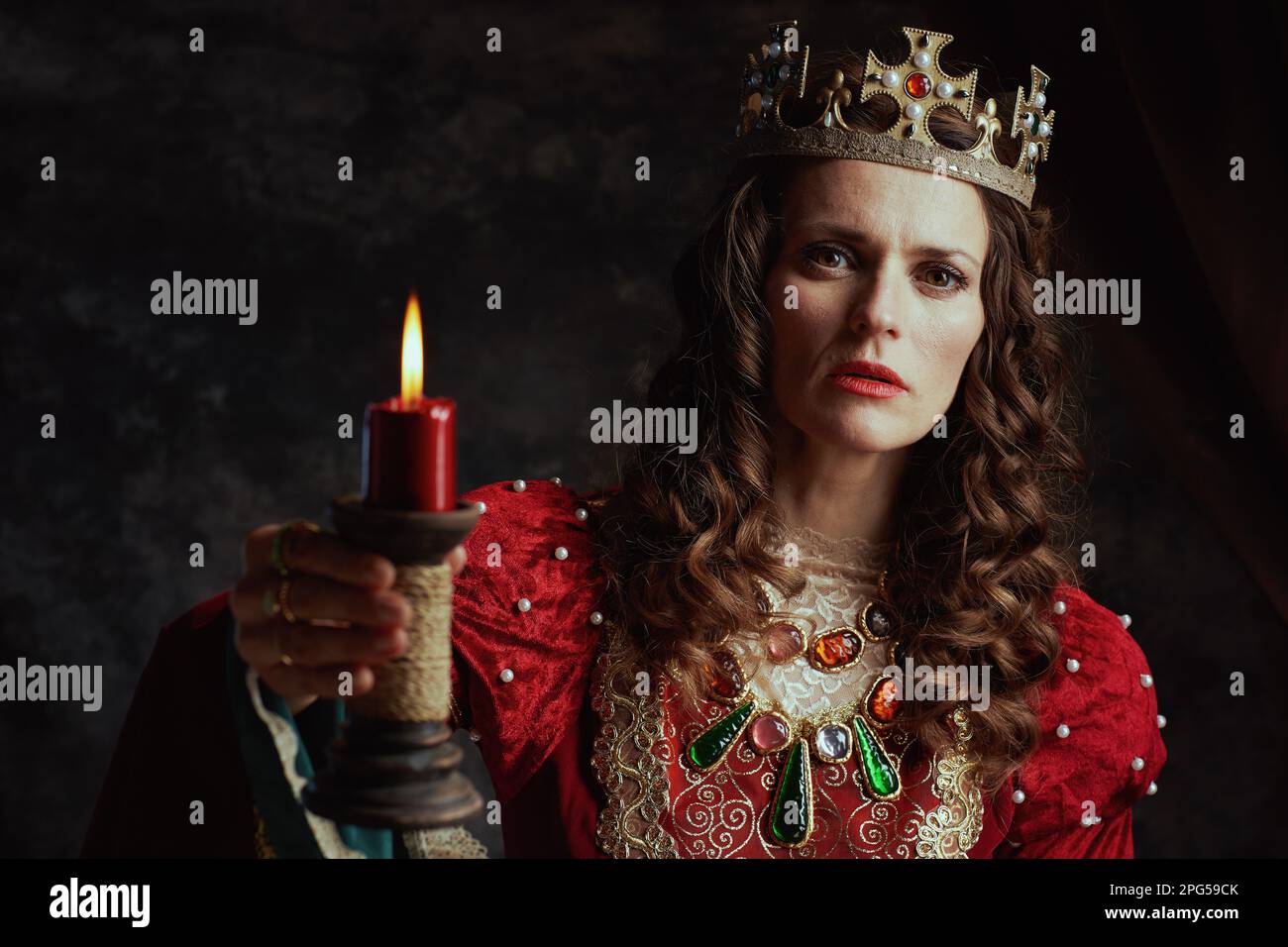 medieval queen in red dress with candle and crown on dark gray ...