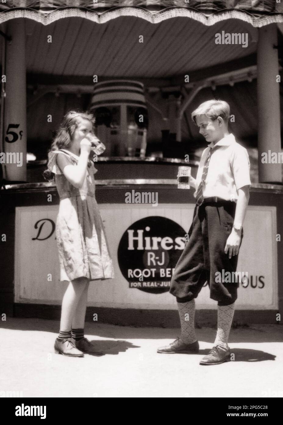 1930s BOY AND GIRL STANDING IN FRONT OF SNACK STAND DRINKING MUGS OF 5 CENT ROOT BEERS SHOWING BRAND NAME HIRES - f7240 HAR001 HARS STYLE TEAMWORK SNACK ABSTRACT PLEASED JOY LIFESTYLE FEMALES BROTHERS SHOWING COPY SPACE FRIENDSHIP FULL-LENGTH PERSONS MALES SIBLINGS SISTERS B&W SUMMERTIME HAPPINESS CHEERFUL ADVENTURE BEVERAGE NAME AND BRAND CENT EXCITEMENT EXTERIOR PRIDE SIBLING SMILES SOFT DRINK CONNECTION BEERS CONCEPTUAL JOYFUL MUGS ROOT STYLISH SUPPORT 5 CENTS GROWTH PRE-TEEN PRE-TEEN BOY PRE-TEEN GIRL SEASON THIRSTY TOGETHERNESS BLACK AND WHITE CAUCASIAN ETHNICITY HAR001 OLD FASHIONED Stock Photo