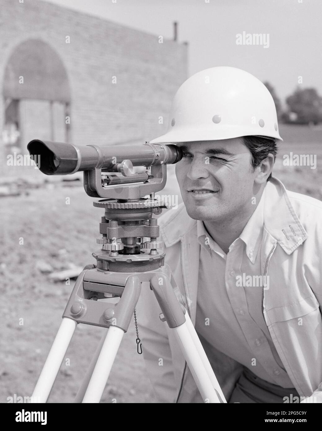 1960s MAN SURVEYOR WEARING HARD HAT USING A THEODOLITE ON CONSTRUCTION SITE i5194 HAR001 HARS