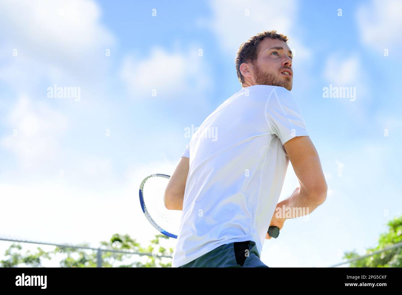 Tennis player man playing game hitting ball finishing serve outdoor. Sport fitness athlete outside with tennis racket. Fit young male caucasian Stock Photo
