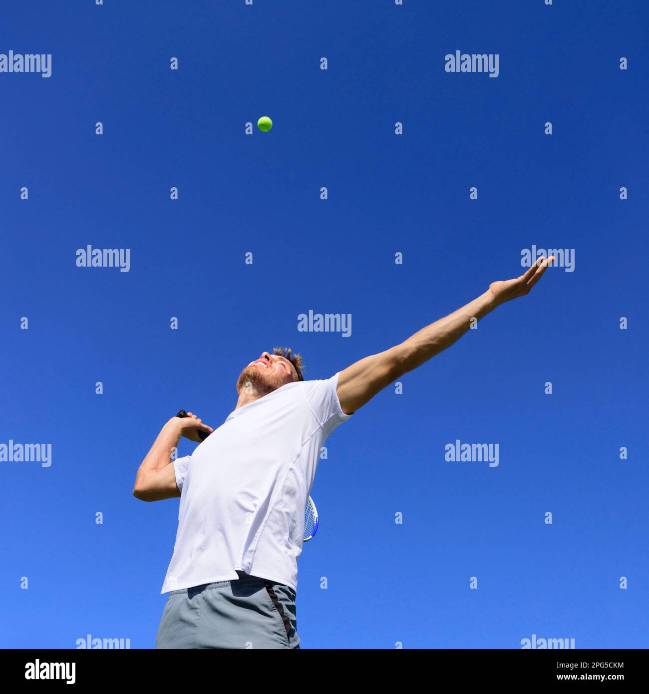 Tennis player man doing serve in position to hit ball in the air. Playing tennis outdoors on blue sky summer background. Active sport athlete doing Stock Photo