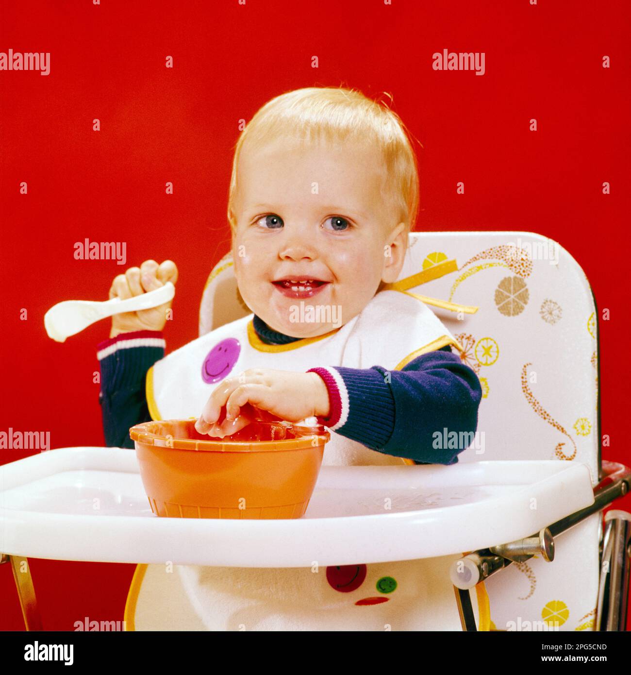 1970s SMILING BLOND BABY BOY LOOKING AT CAMERA SITTING IN HIGH CHAIR RIGHT HAND HOLDING SPOON LEFT STICKING HAND INTO FOOD BOWL - kb10042 HAR001 HARS FACIAL LAUGH BLOND INFANT PLEASED JOY LIFESTYLE SATISFACTION STUDIO SHOT HEALTHINESS HOME LIFE COPY SPACE MALES EXPRESSIONS HAPPINESS HEAD AND SHOULDERS CHEERFUL STICKING IN INTO RIGHT SMILES JOYFUL BABY BOY CHARMING GROWTH HIGH CHAIR JUVENILES LEFT CAUCASIAN ETHNICITY HAR001 OLD FASHIONED Stock Photo