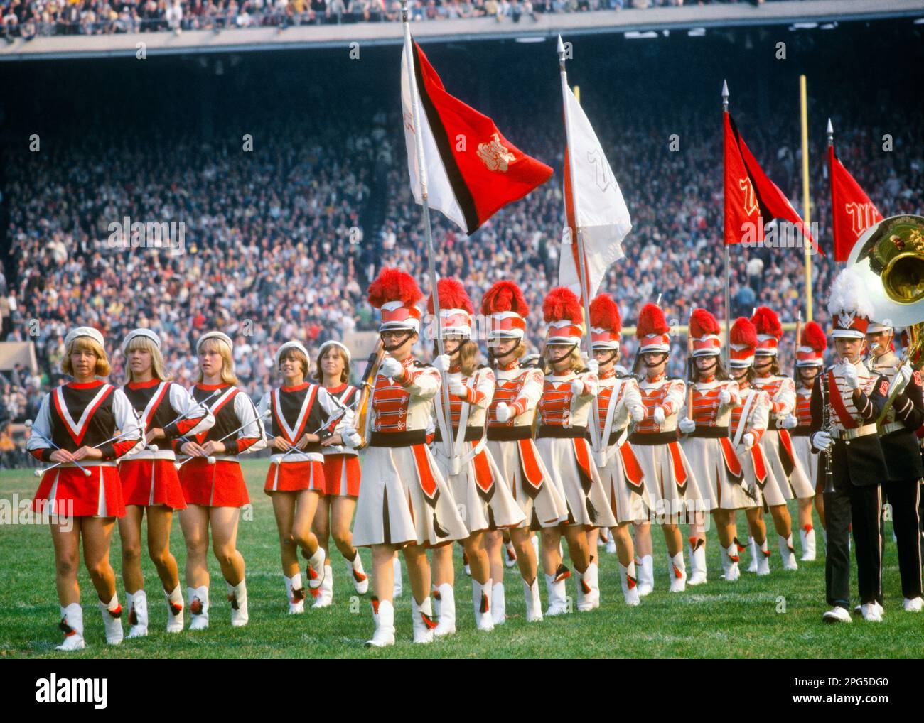 1960s MARCHING BAND AND MAJORETTES COLOR GUARD PARADE ON FOOTBALL FIELD