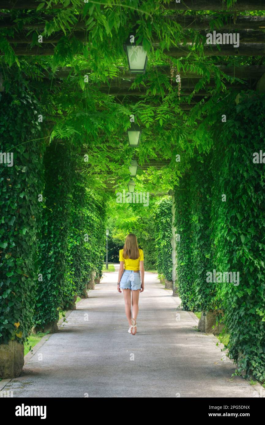 Green trees alley and young woman in blooming park in summer Stock Photo