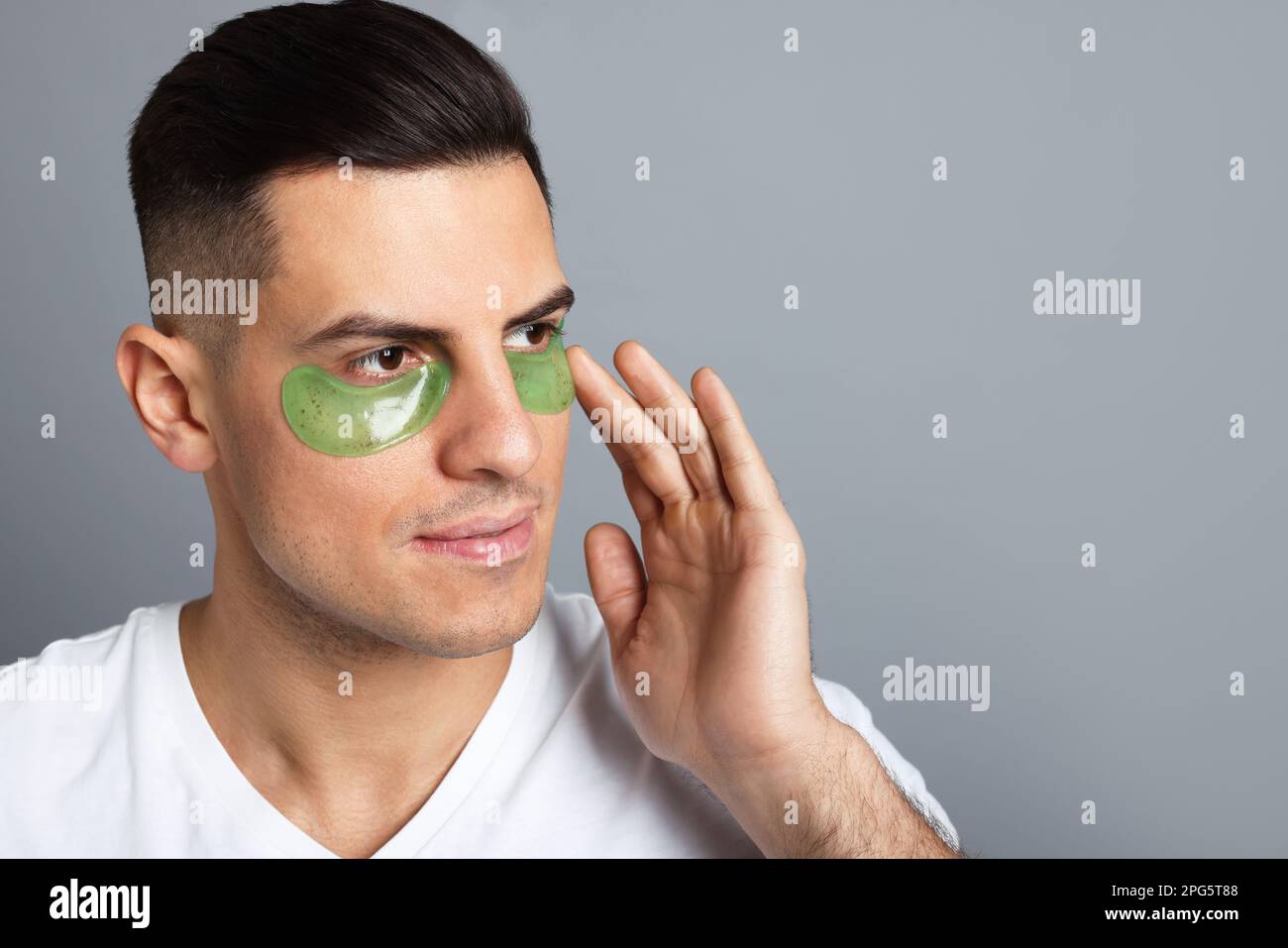 Man applying green under eye patch on grey background. Space for text