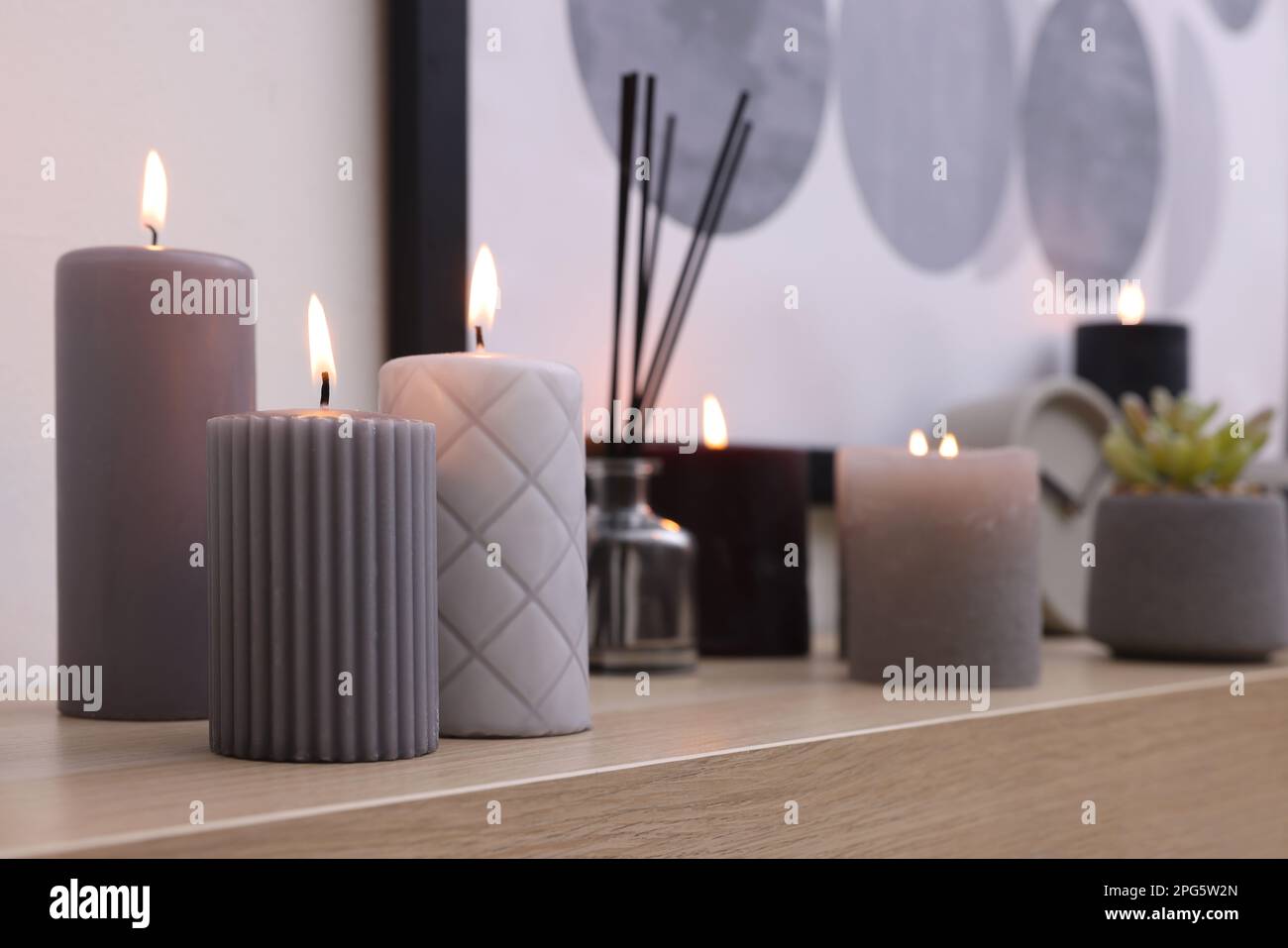 Burning candles and air freshener on wooden shelf indoors Stock Photo