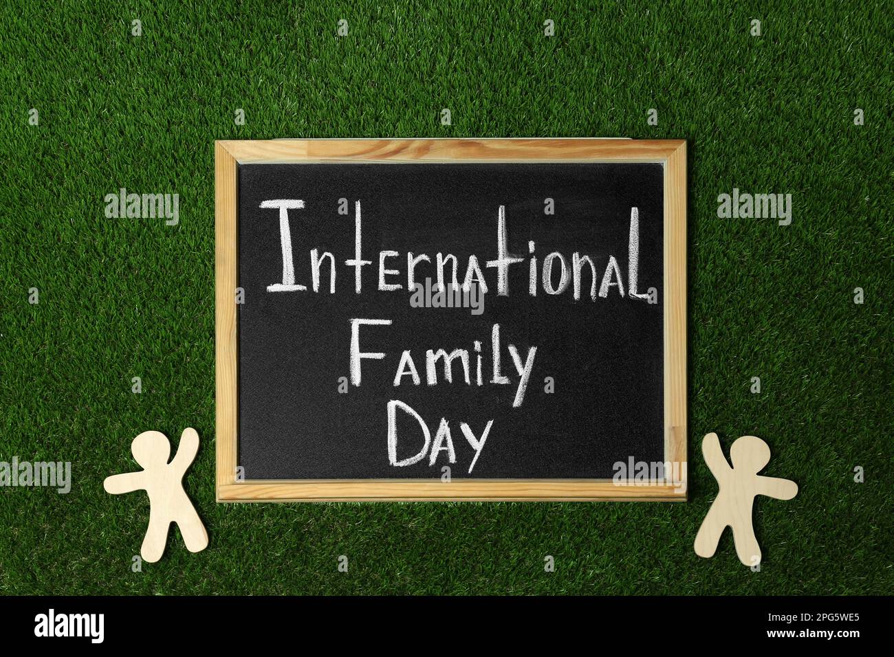 Chalkboard with text International Family Day and wooden figures on green grass, flat lay Stock Photo