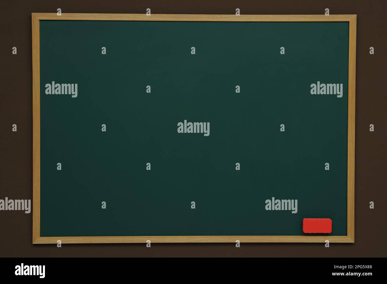 Clean green chalkboard with duster hanging on brown wall Stock Photo