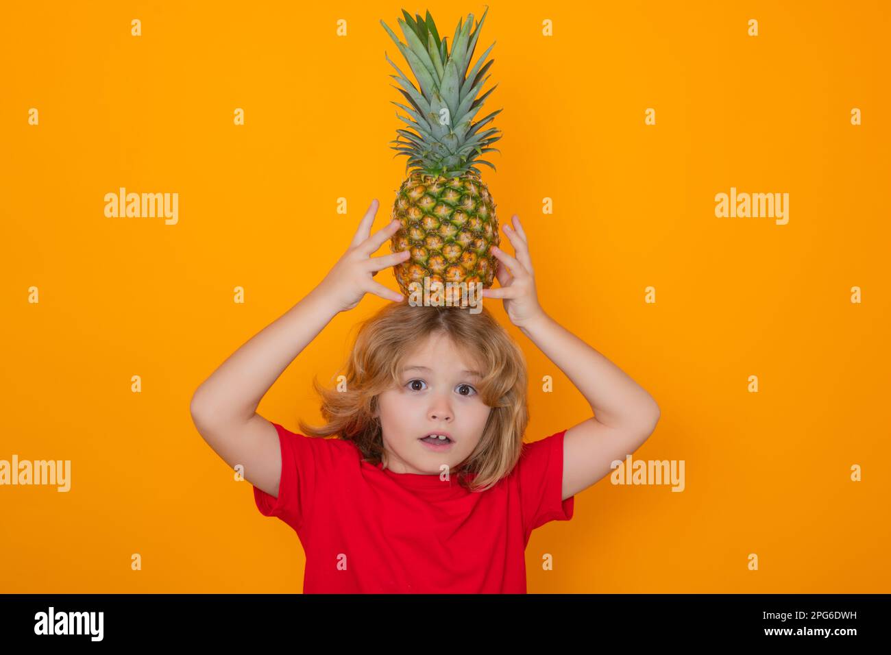 Kid with pineapple in studio. Studio portrait of cute child hold pineapple isolated on yellow background Stock Photo
