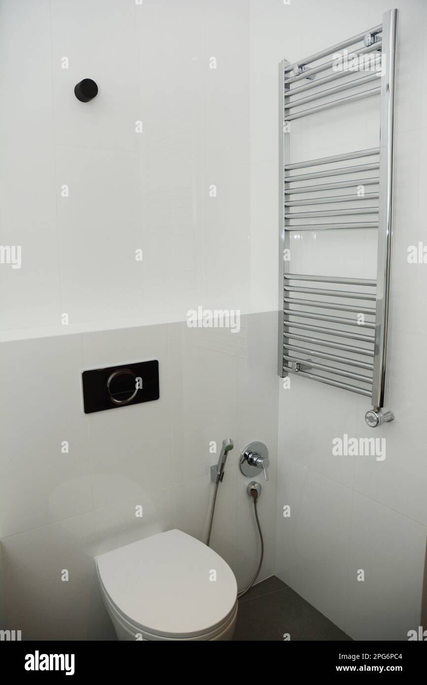 White toilet bowl with bidet shower and thermostatic electric towel rail in modern bathroom. Stock Photo