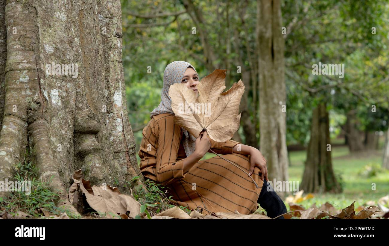Muslim girl sitting and covering her face with dried leave in the 