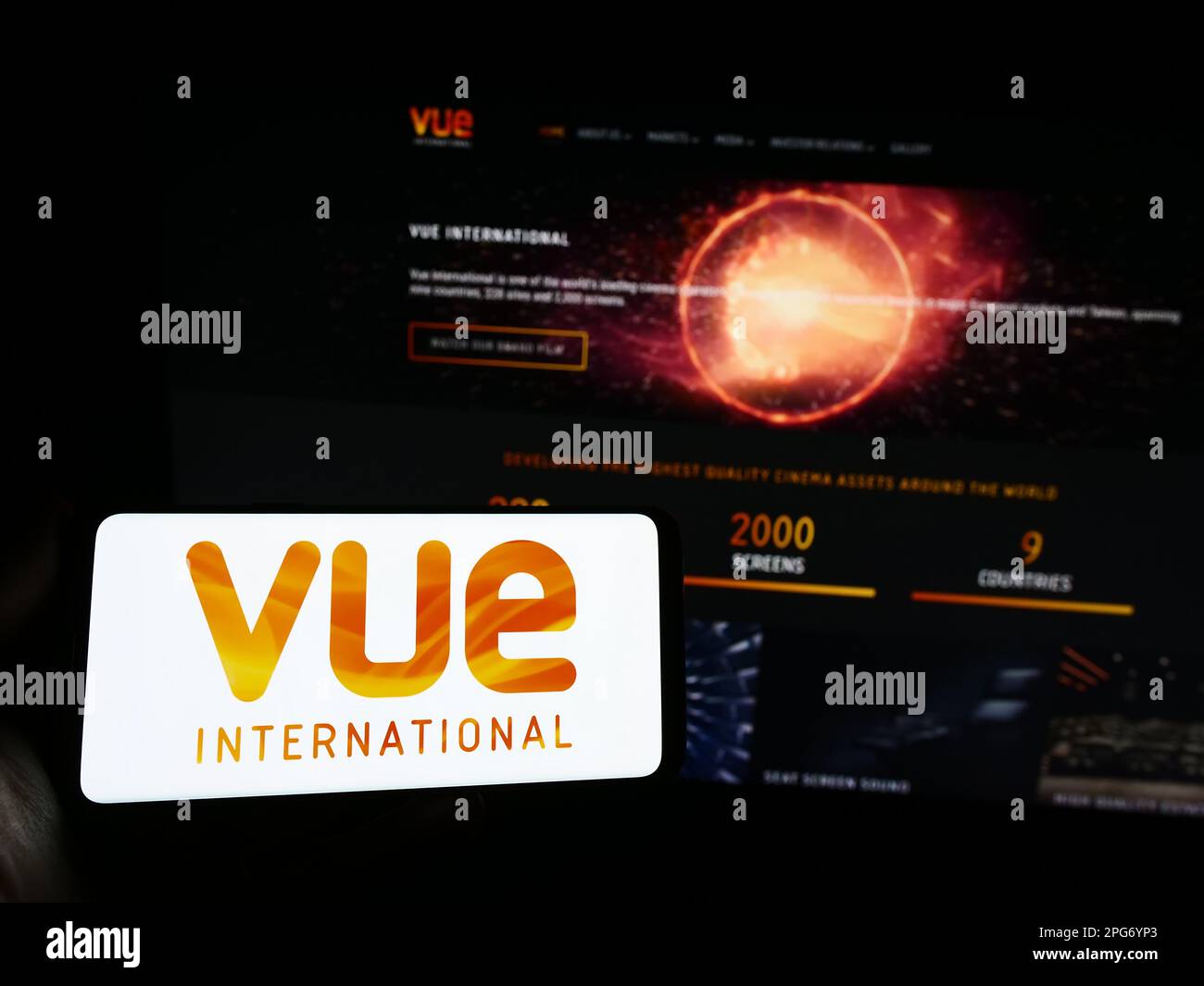 Person holding smartphone with logo of entertainment company Vue International on screen in front of website. Focus on phone display. Stock Photo
