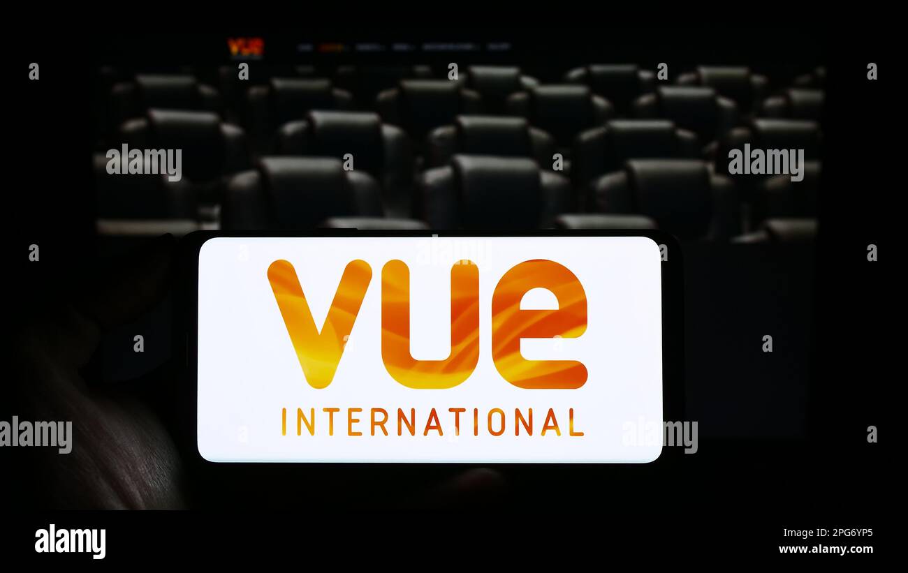 Person holding mobile phone with logo of entertainment company Vue International on screen in front of business web page. Focus on phone display. Stock Photo