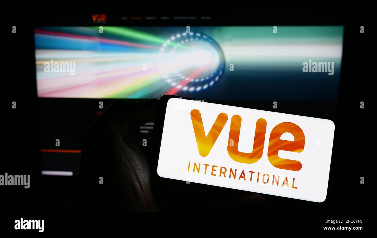 Person holding cellphone with logo of entertainment company Vue International on screen in front of business webpage. Focus on phone display. Stock Photo