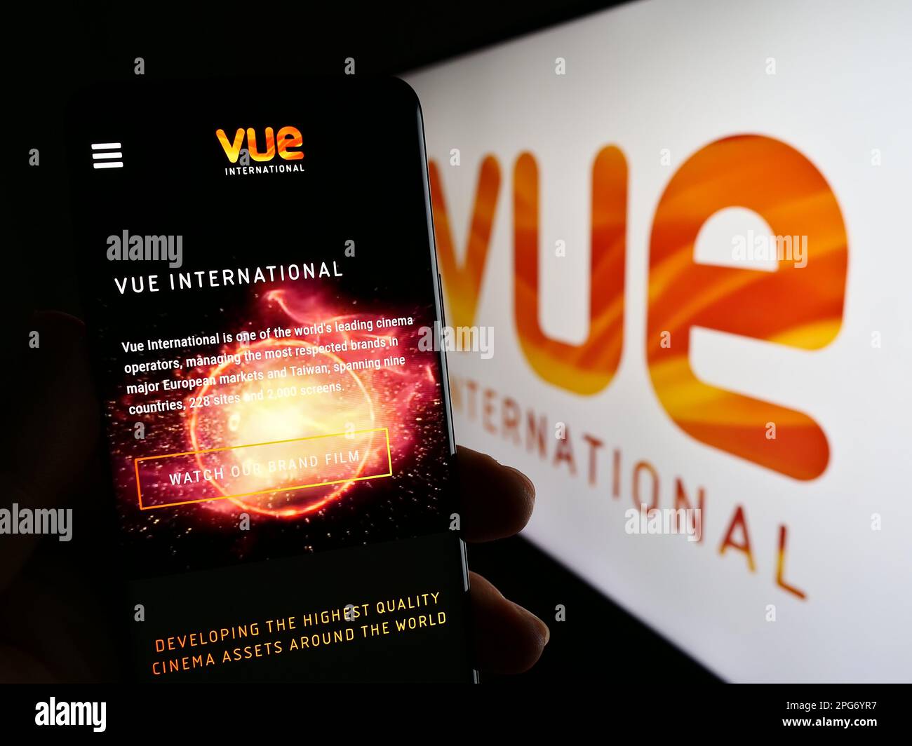 Person holding smartphone with website of entertainment company Vue International on screen in front of logo. Focus on center of phone display. Stock Photo