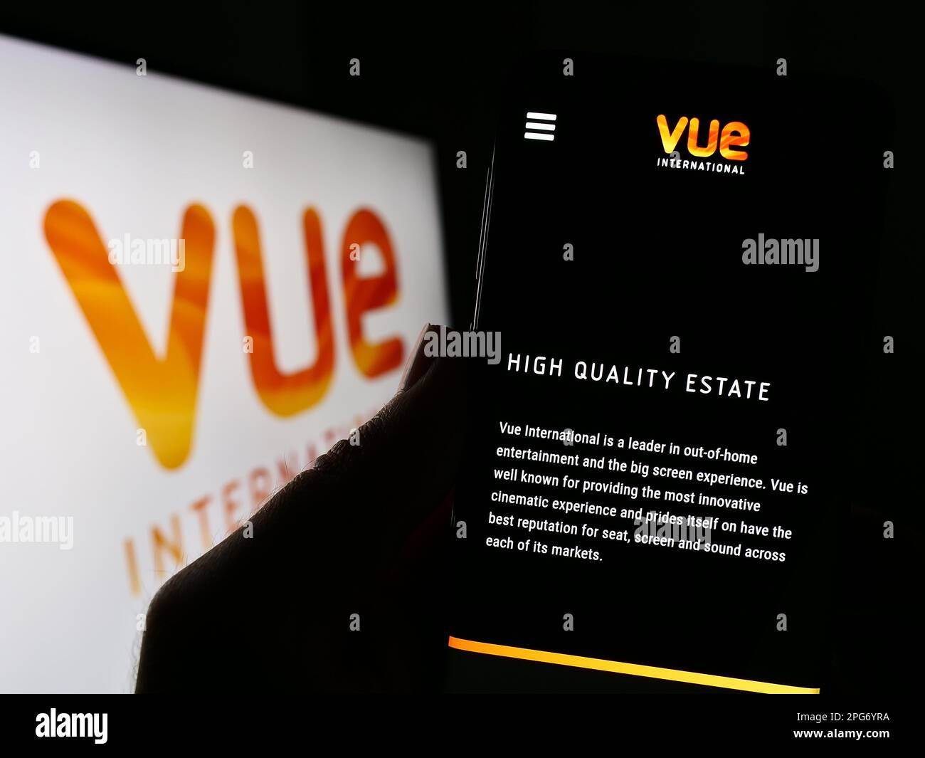 Person holding cellphone with webpage of entertainment company Vue International on screen in front of logo. Focus on center of phone display. Stock Photo
