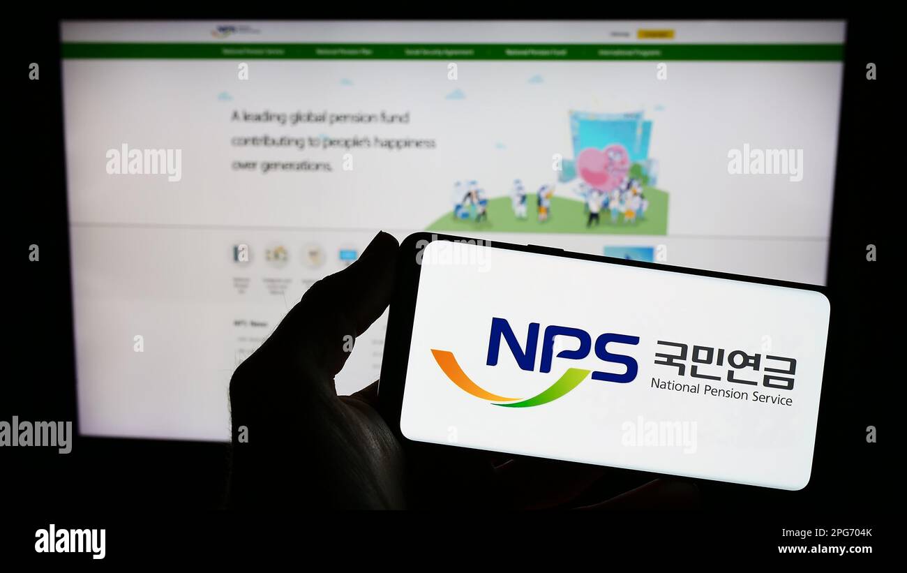 Person holding smartphone with logo of National Pension Service of Korea (NPS) on screen in front of website. Focus on phone display. Stock Photo