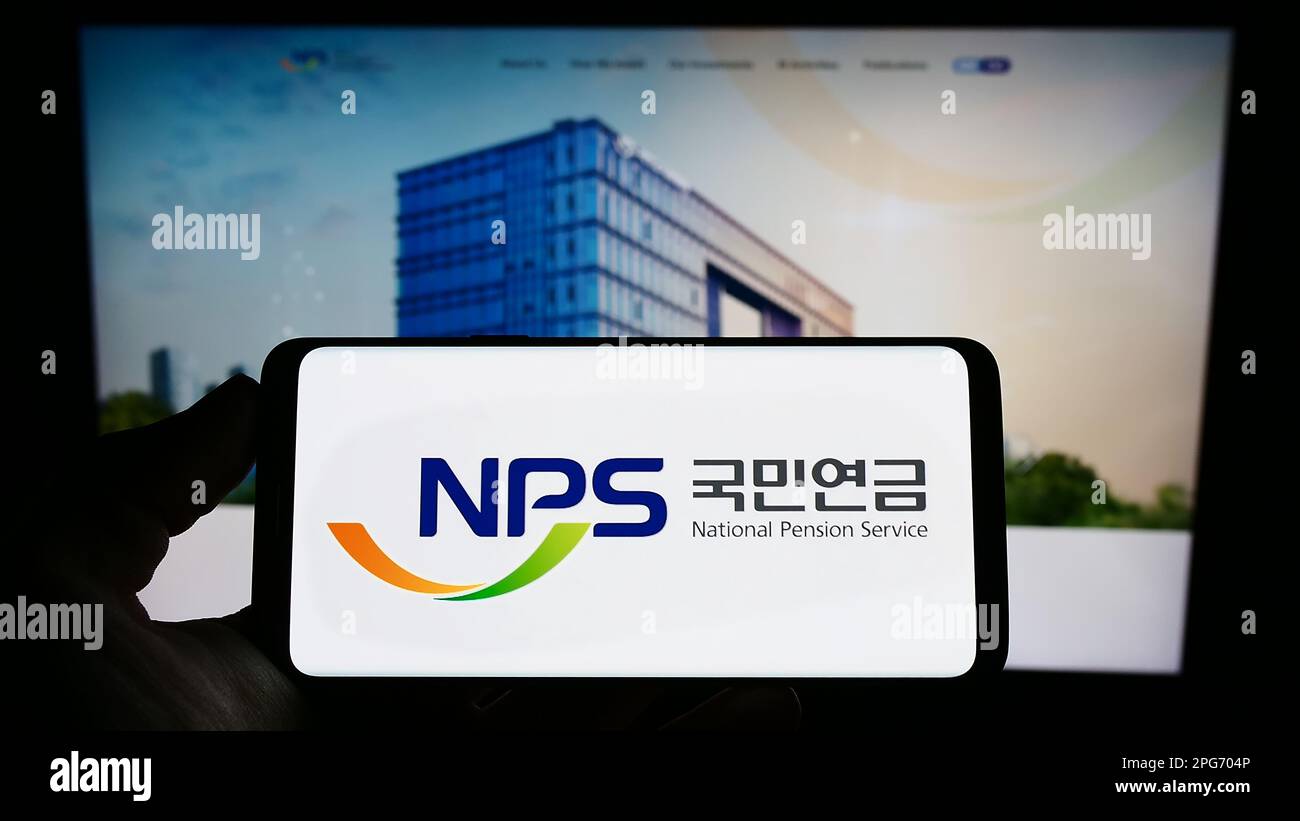 Person holding cellphone with logo of National Pension Service of Korea (NPS) on screen in front of webpage. Focus on phone display. Stock Photo